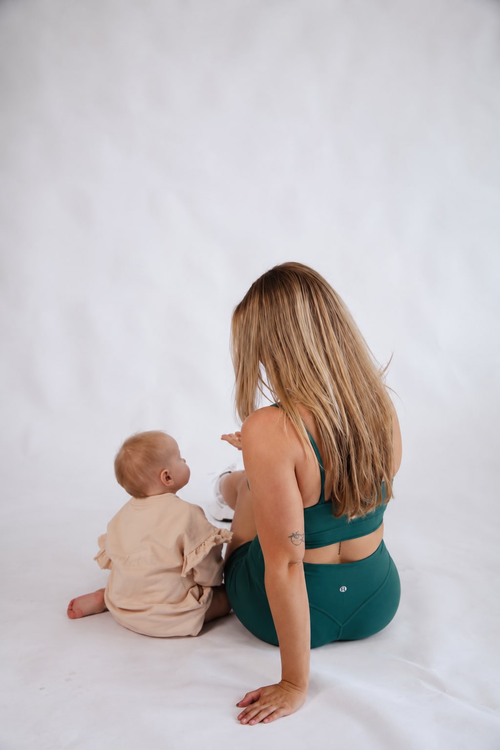 Madison and her baby daughter sitting side by side on the studio floor, seen from behind.
