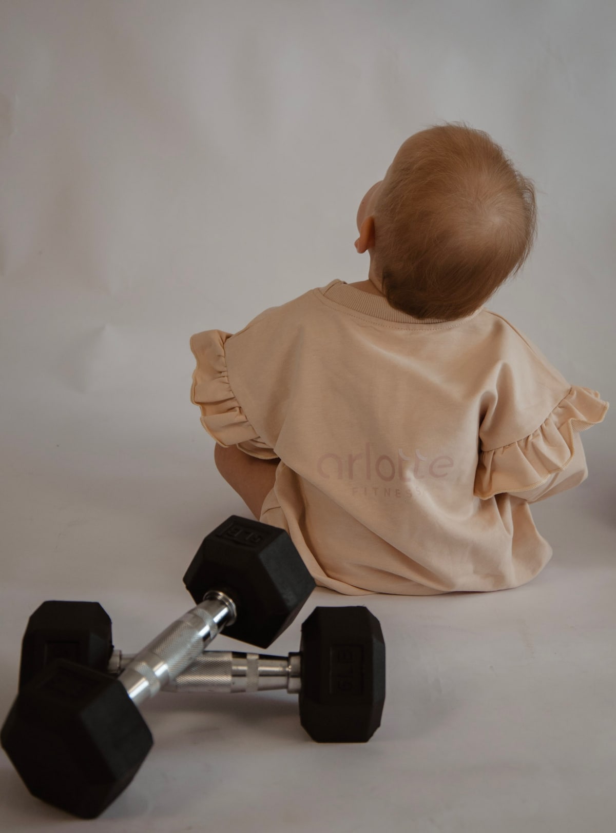 Madison's baby daughter, seen from behind, sitting beside a pair of hex dumbbells.