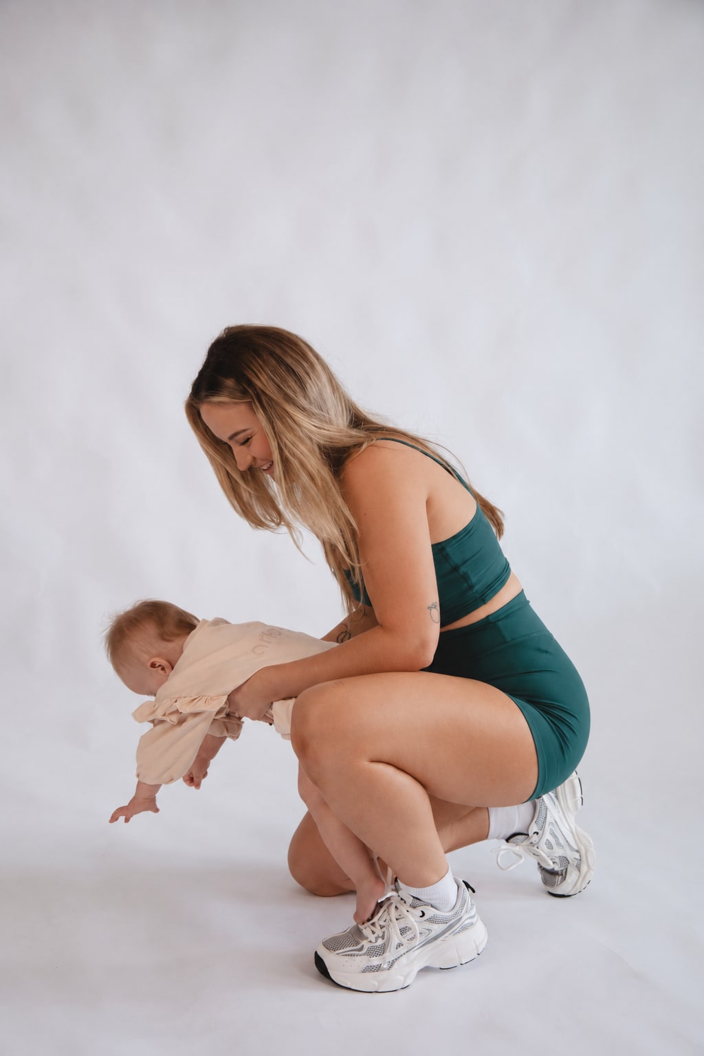 Madison crouching on the studio floor, helping her baby daughter stand.