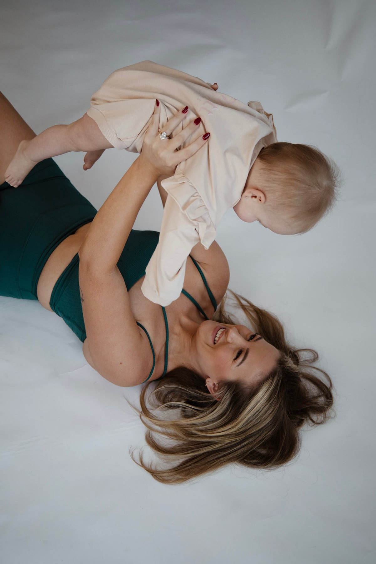 Madison lying on her back, lifting her laughing baby daughter overhead.